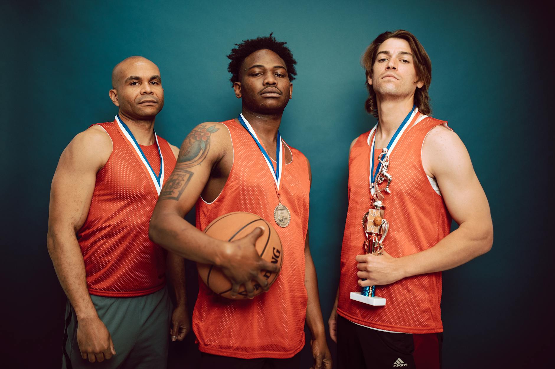 Three basketball players posing confidently with medals and a trophy in a studio.