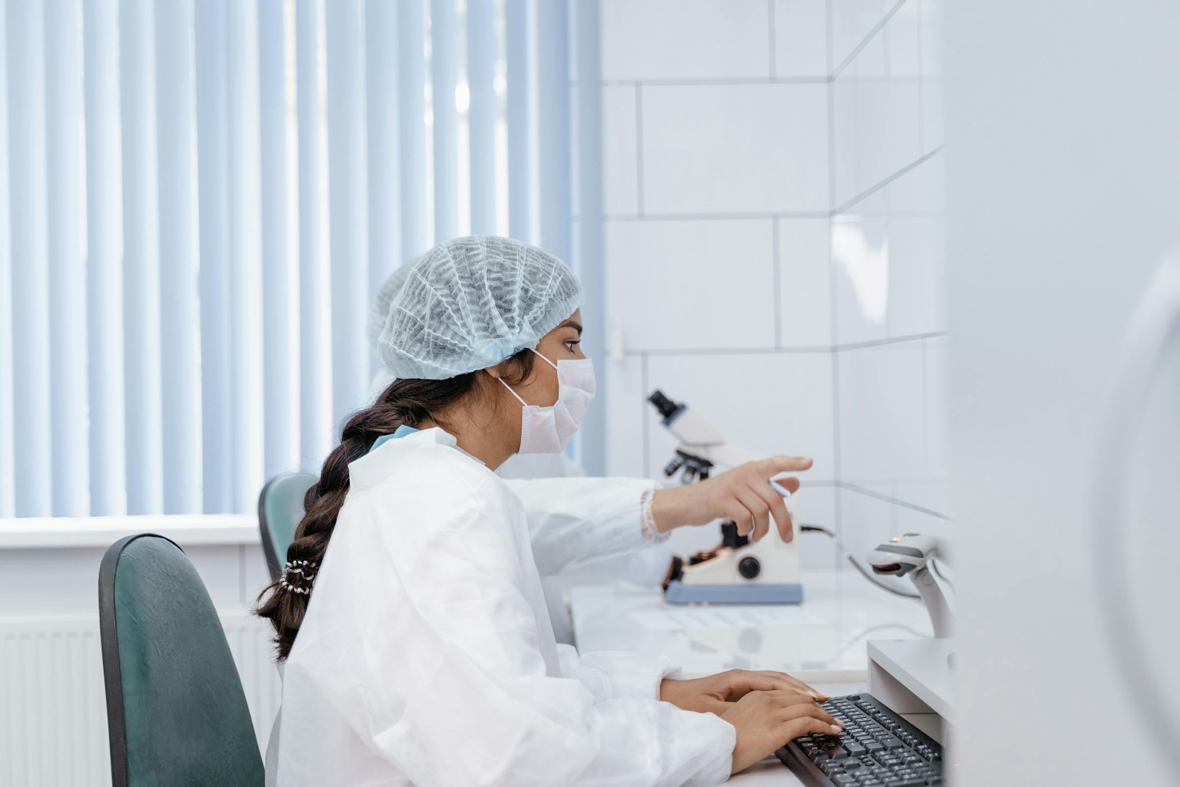 Scientist in laboratory coat working at computer in a pharmaceutical research lab.